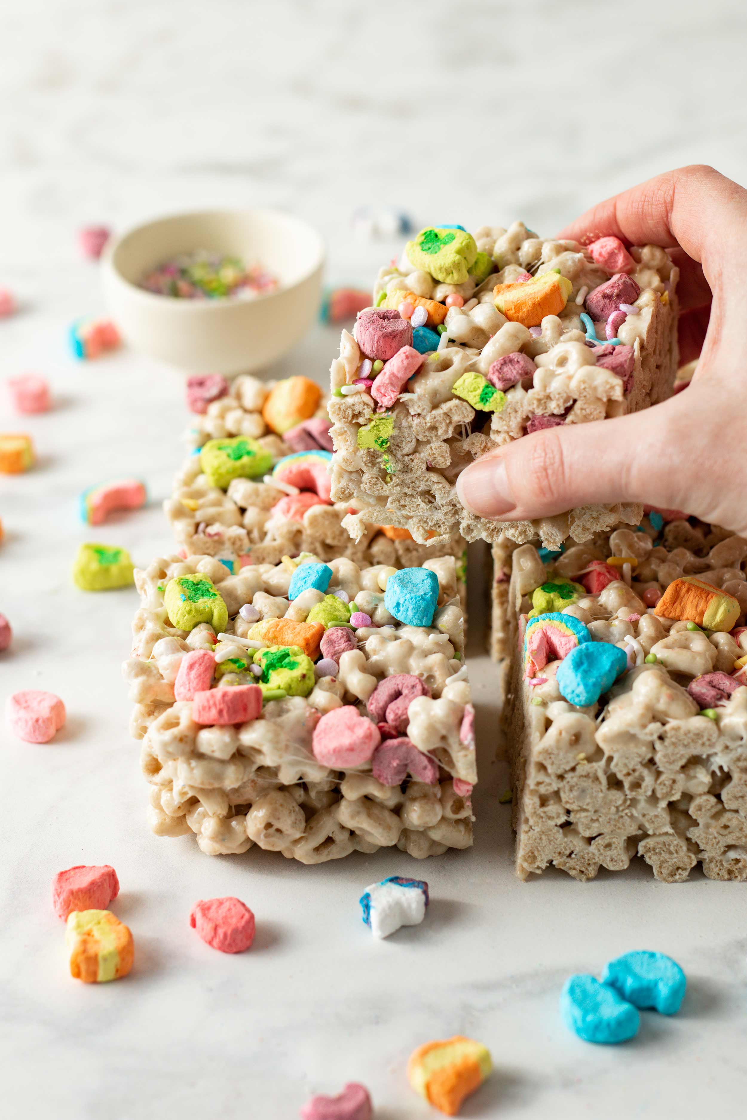 Hand reaching for a Lucky Charms Marshmallow Crispy Treats square